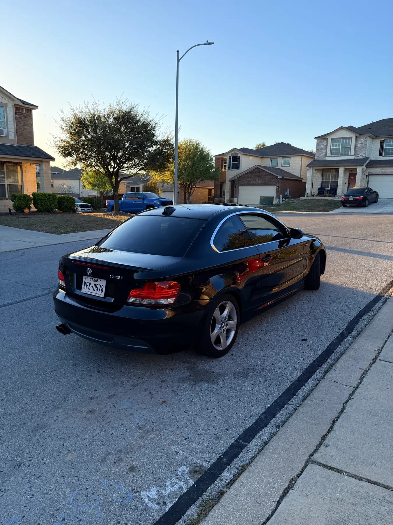 The same black BMW 135i from behind, rear three-quarter, tail lights and rear glass clean.