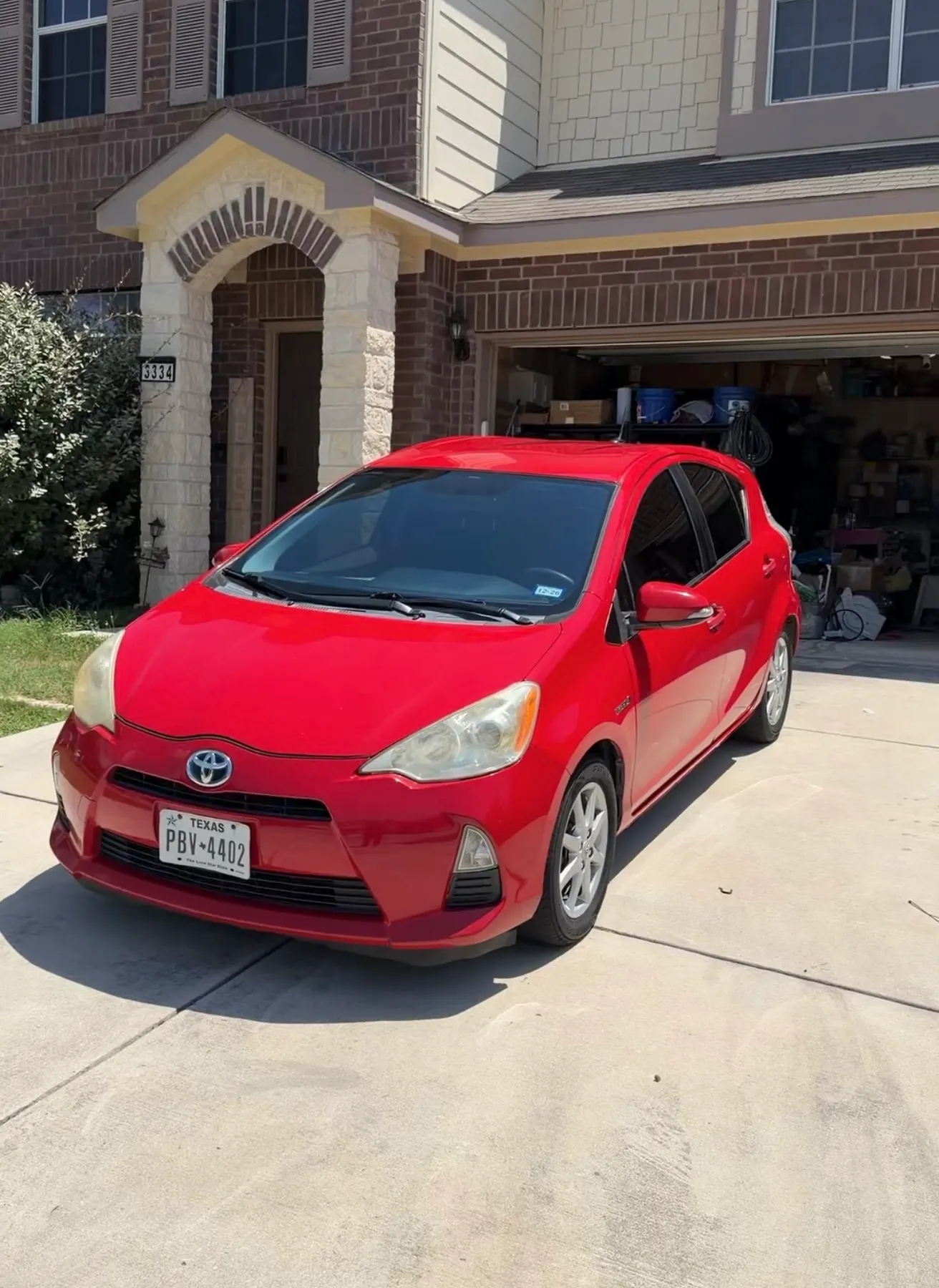 A red Toyota Prius c on a driveway after a full detail, paint clean and glossy in full sun.
