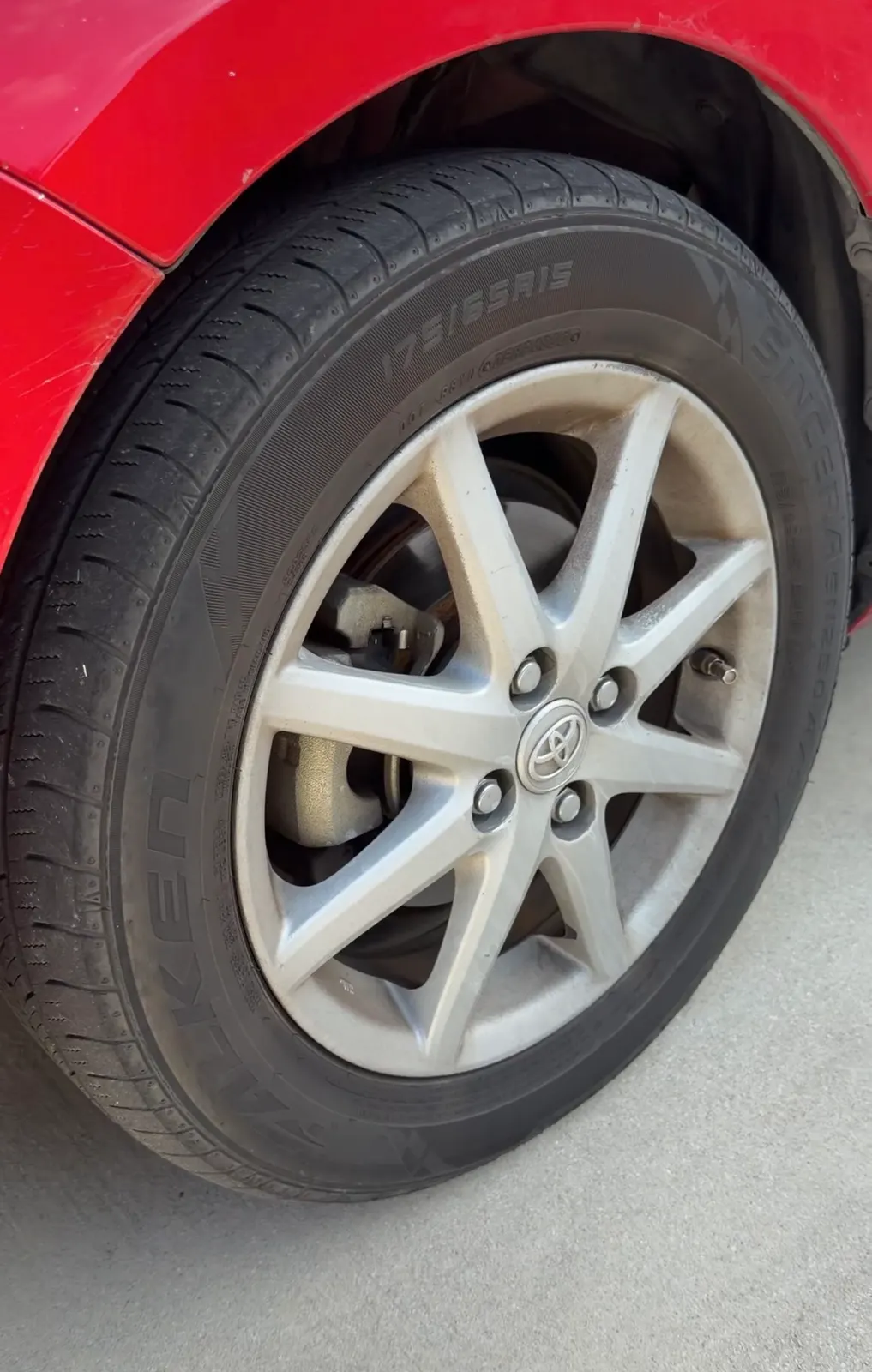 The Prius's front driver wheel before work, brake dust across the spokes and grime worked into the barrel.